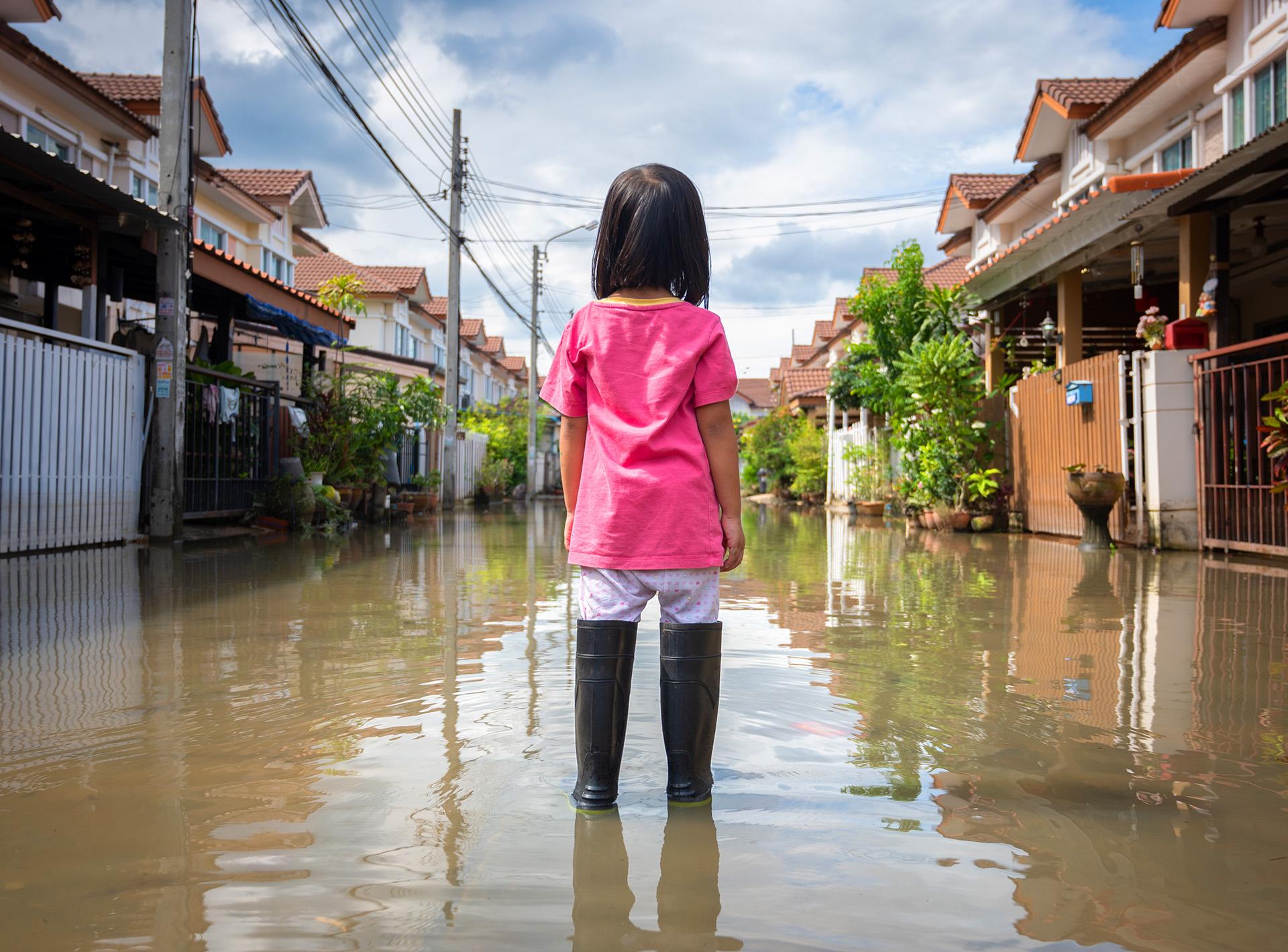 Young girl in standing water, facing flooded street.